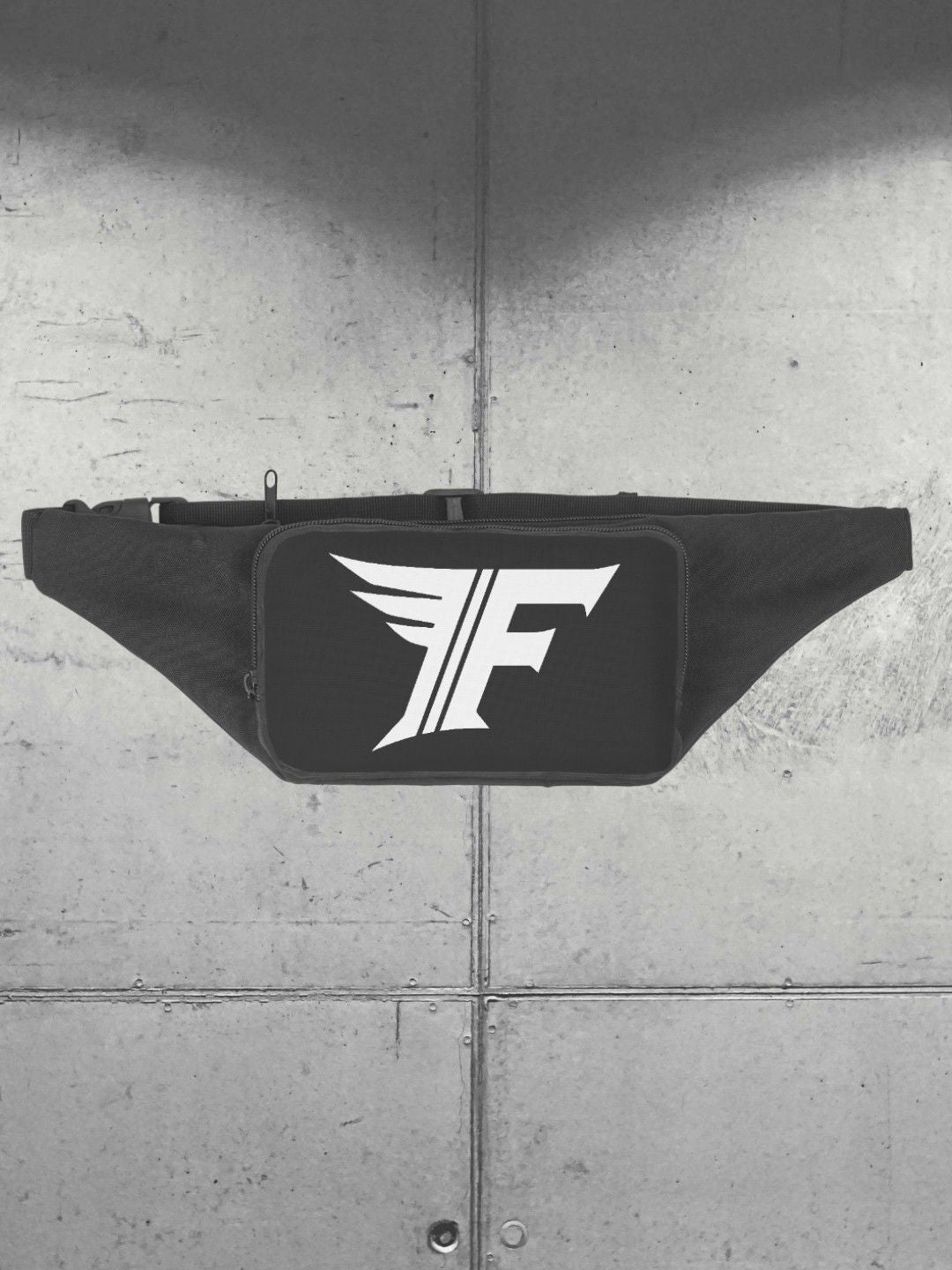 Frontal view of a black zippered waist bag, emphasizing the white 'F' logo. Shot against a gray, industrial background texture.